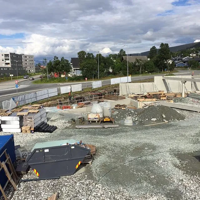 Byggeplass med betongkonstruksjoner og materialer ved rundkjøring i byområde.