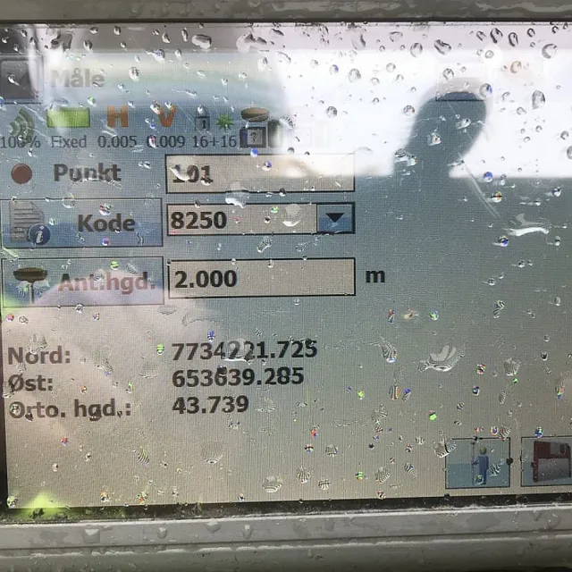 Nærbilde av en våt GPS-enhet fra Topcon med koordinatdata på skjermen.