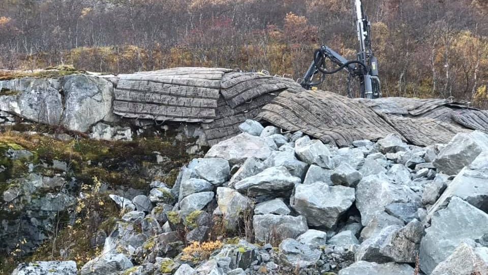 Fjellside med store steiner og beskyttelsesmatter, borerigg i bakgrunnen.