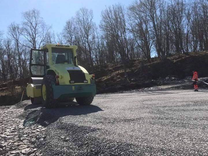 Veivals og arbeider med løvblåser jevner og rydder gruslagt område ved skogkant.