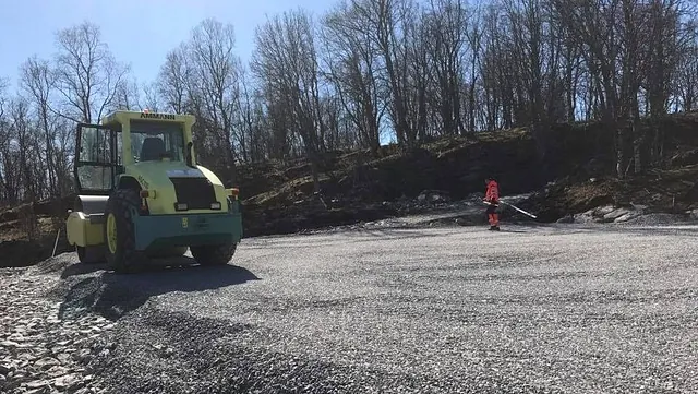 Veivals og arbeider med løvblåser jevner og rydder gruslagt område ved skogkant.